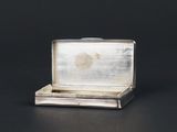 a small silver box with a silver lid on a black surface