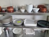 Plusieurs assiettes et bols sont empilés sur une étagère en métal dans une cuisine