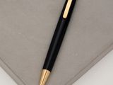 black and gold ballpoint pen laying on top of a gray surface