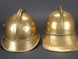 pair of antique brass fire helmets on a black background