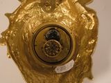 a gold clock that is on a white wall