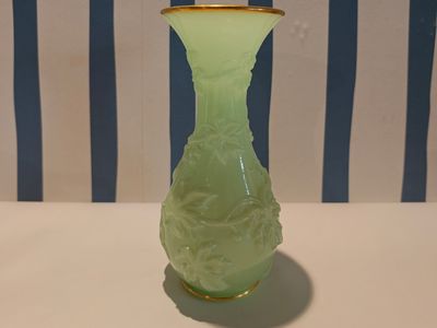 a green vase with a gold rim sitting on a table