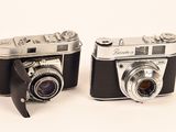 two old cameras sitting next to each other on a white surface