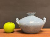a green apple next to a blue vase on a wooden table