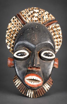 une image représentant un masque en bois au visage noir et coiffé d'une parure dorée