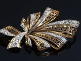 an image of a gold and diamond bow broochle on a black surface