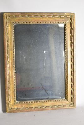 un miroir à cadre doré accroché au mur, à côté d'un mur blanc