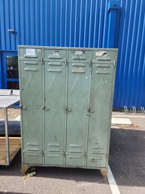 une armoire métallique verte dans un parking, à côté d'un bâtiment bleu