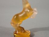 un cheval en verre posé sur un socle jaune, lui-même posé sur une surface grise