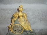 a gold clock with a woman sitting on top of it