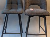 pair of grey upholstered bar stools against a white wall