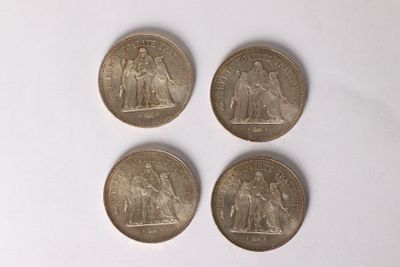 four coins are shown on a white surface, one of which has a picture of a woman and two men