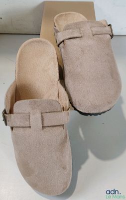 une paire de sabots en daim beige avec des boucles, posée sur une boîte en carton