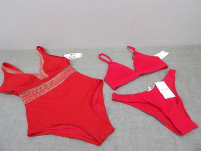 two pieces of red swimsuits on a bed with a price tag