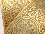 two gold cuff bracelets with intricate designs on them on a white surface