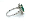 an oval emerald and diamond ring on a white surface