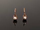 une paire de boucles d'oreilles en perles et en or posées sur une surface réfléchissante