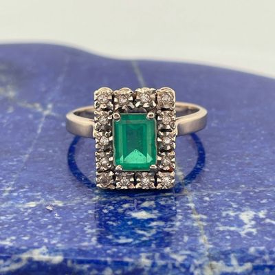 une bague sertie d'une émeraude et de diamants repose sur une pierre bleue