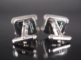 two silver cufflinks with black and white squares on them