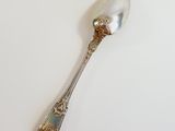 a silver spoon on a white surface with a gold decoration on it