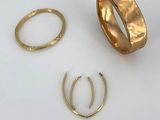 three gold rings and two gold hoops on a white surface