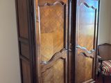 a wooden armoire in a room with a striped chair
