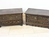 une paire de coffres anciens en bois sculpté, posés sur des roulettes, sur un sol carrelé