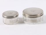 two small glass jars with silver lids sitting on a white surface