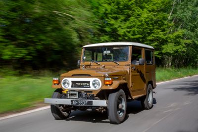 a brown jeep driving down the road with trees in the background