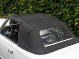 a white car with a black top parked in front of a hedge