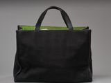 a black tote bag with green handles on a white surface