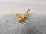 une photo représentant une broche en forme d'oiseau de couleur dorée posée sur une couverture grise