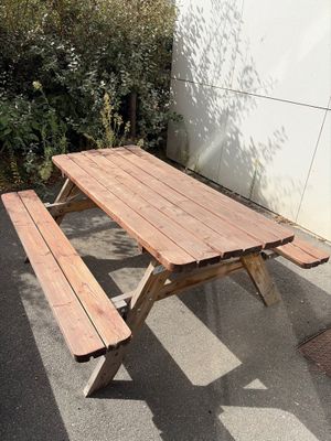 une table de pique-nique en bois avec deux bancs, devant un mur blanc