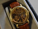 a gold watch with a brown leather strap in a box