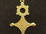 a gold pendant with a cross on it on a black surface