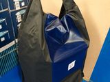 un sac noir posé sur un sol bleu, à côté d'une pile de cartons