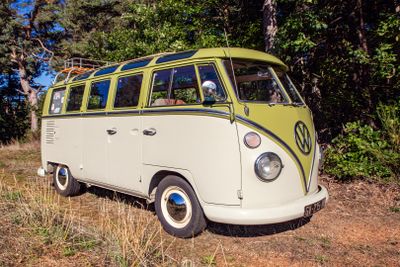 un minibus Volkswagen jaune et blanc garé dans un champ, avec des arbres en arrière-plan