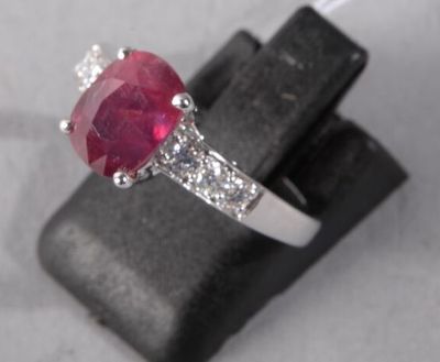 an oval ruby and diamond ring on top of a black piece of wood