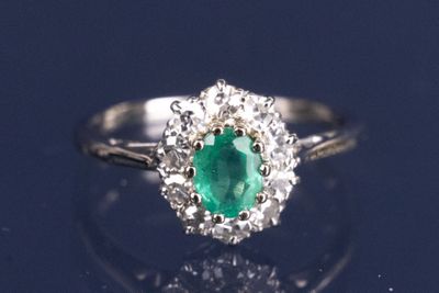 une bague ovale sertie d'une émeraude et de diamants posée sur une surface réfléchissante
