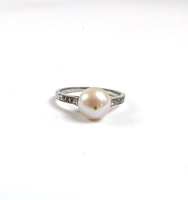 une bague en perle blanche et diamants posée sur une surface blanche