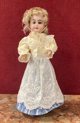 une poupée ancienne en porcelaine représentant une jeune fille vêtue d'une robe blanche et d'une jupe bleue