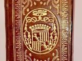 an old book with a gold and red cover sitting on a white surface