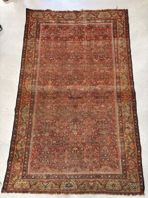 un tapis persan ancien posé sur un sol blanc, à côté d'un fauteuil