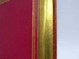 an old red book with gold trim sitting on top of a wooden table
