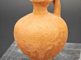 un vase en argile posé sur un socle en verre