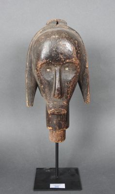 un gros plan d'un masque en bois posé sur un socle, sur fond gris