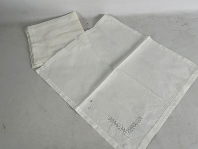 deux serviettes de table en lin blanc ornées de motifs brodés, posées sur une table
