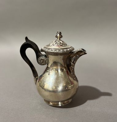 une cafetière ancienne en argent avec une poignée noire, posée sur une table