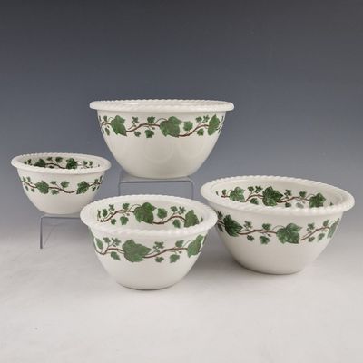 quatre bols blancs ornés de motifs de lierre vert, posés sur une table