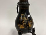 une image représentant un vase noir et doré posé sur un socle